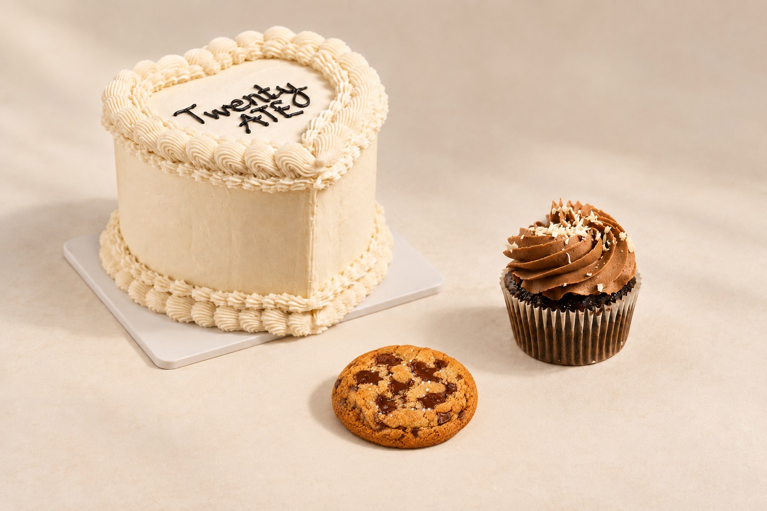 Styled collection image of an ivory celebration cake, chocolate chip cookie and chocolate cupcake