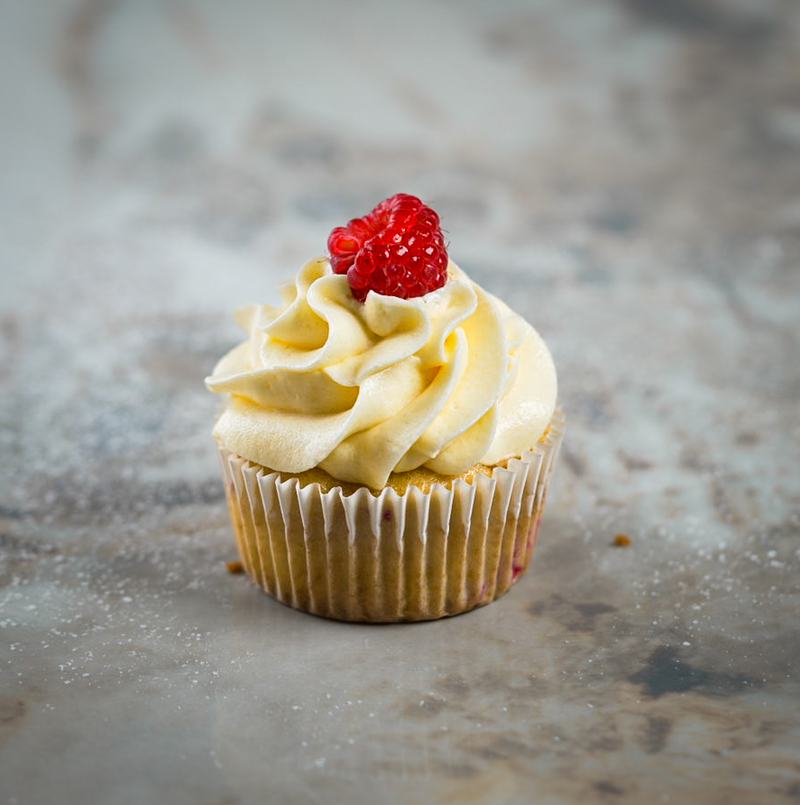 Cupcake topped with vanilla buttercream and a fresh raspberry